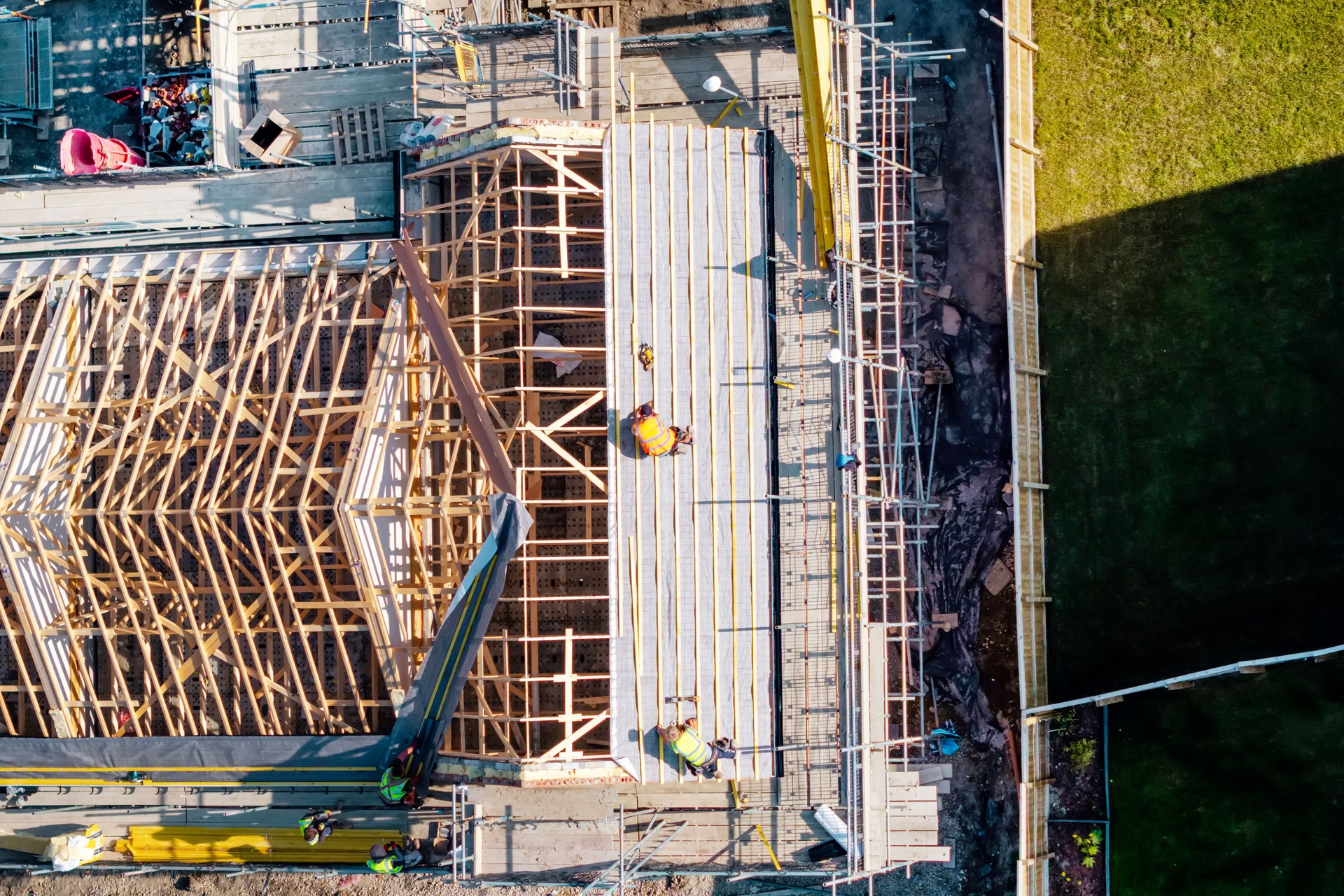 Aerial view from drone at construction workers actively engaged in building roof structure with wooden framework during daylight hours