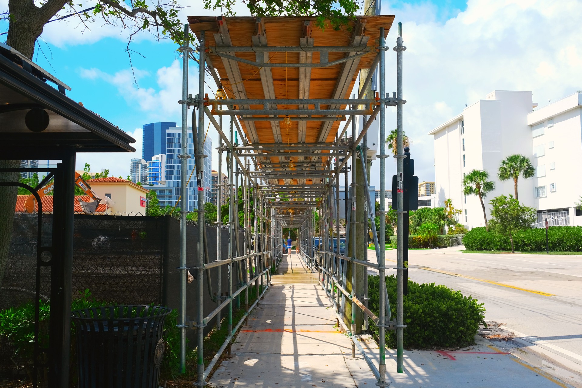 Construction scaffolding on pedestrian sidewalk walkway on city street on summer day urban street view photo. Renovation, reconstruction work. Construction site industrial structure.