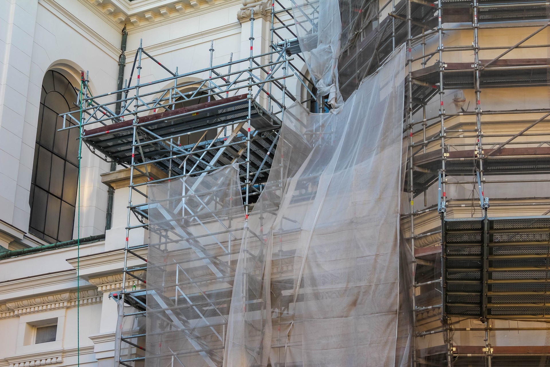 Classical building entrance with ornate columns wrapped in transparent protective plastic during restoration process